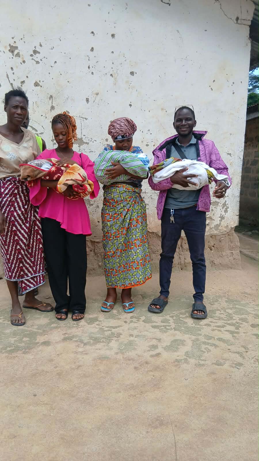 The mother in a pink blouse and two relatives hold the swaddled triplets outside the family home.