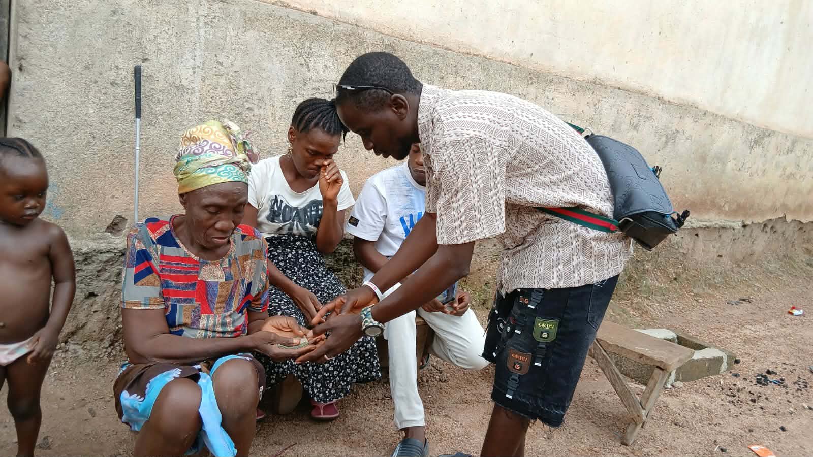 A Lofa24 team member counts money into the grandmother's open hands as her daughter and grandson look on.